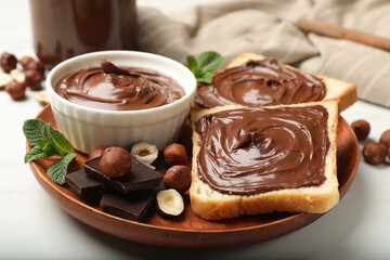 Toasts with chocolate hazelnut spread, nuts, pieces of chocolate and mint on white table, closeup