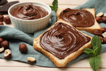 Toasts with chocolate hazelnut spread, nuts and mint on wooden table, closeup