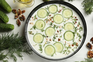 Fresh tasty cucumber soup and ingredients on white table, flat lay