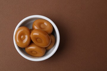 Tasty sweet caramel candies on brown background, top view. Space for text