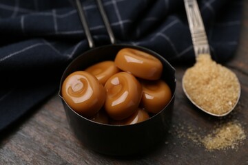 Tasty sweet caramel candies and sugar on wooden table, closeup