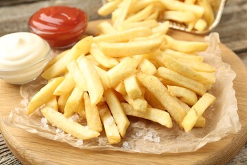 Tasty french fries served with sauces on wooden table, closeup