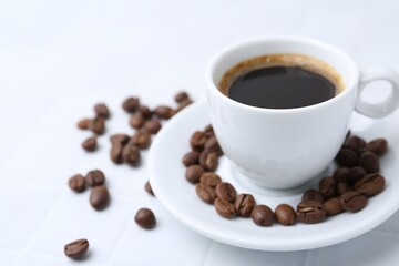 Aromatic coffee in cup and beans on white table, closeup. Space for text