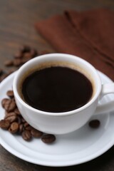 Aromatic coffee in cup, beans and saucer on wooden table, closeup