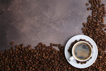 Aromatic coffee in cup, saucer and beans on brown textured table, flat lay. Space for text