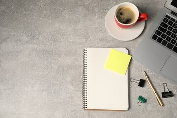 Notebook, pen, sticky note, binder clips, coffee and laptop on grey table, flat lay. Space for text