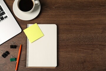 Notebook, pen, sticky note, binder clips, coffee and laptop on wooden table, flat lay. Space for text