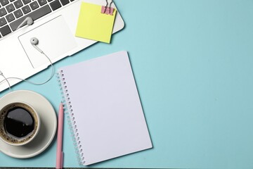 Notebook, pen, sticky note, earphones, coffee, binder clip and laptop on light blue background, flat lay. Space for text