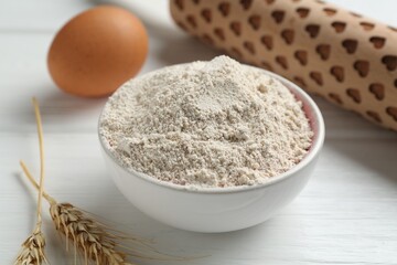 Flour in bowl, rolling pin, egg and spikes on white wooden table, closeup