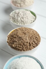 Different types of flour in bowls on white wooden table, closeup