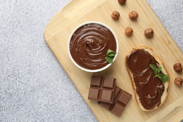 Tasty chocolate spread, toast, hazelnuts and mint on grey textured table, top view. Space for text