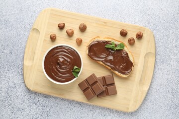 Tasty chocolate spread, toast, hazelnuts and mint on grey textured table, top view