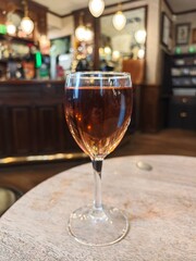 Elegant glass of rich amber beverage rests on a rustic wooden table in a charming tavern filled...