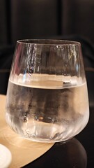 Elegant glass filled with clear water resting on a wooden table, reflecting soft ambient lights in a cozy interior setting