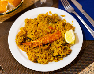 Traditional Valencian paella de mariscos with shrimps, calamaries and mussels served with lemon slice on white plate..