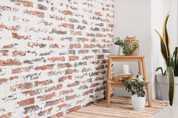 Stool with books, candles and plants near brick wall in room
