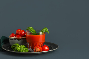 Glass of fresh tomato juice with basil and vegetables on dark background