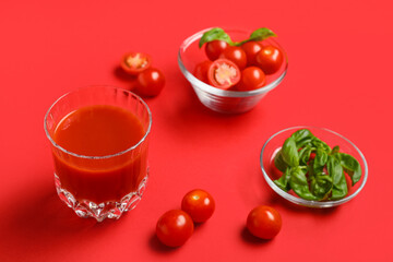 Glass of fresh tomato juice with basil and vegetables on red background, closeup