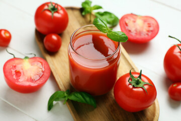Glass of fresh tomato juice with basil and vegetables on white wooden background, closeup
