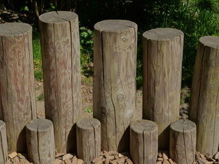 Natural wooden logs arranged vertically as playground steps, outdoors in a forest park setting. Rustic nature-inspired play equipment with bark chips on the ground