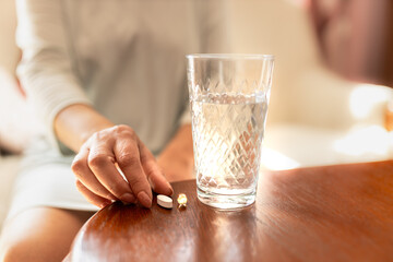 Adult woman holding a pill and a glass of water. Female taking medicine. Treating at home. Patient recovering in a hospital. Mental health