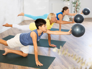 Positive preteen boy practicing balancing table pose of yoga holding softball in hand in fitness...