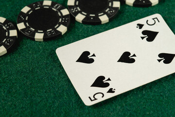 A five of spades card lies on green felt alongside several black and white poker chips. This setup...
