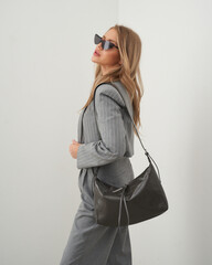 Blonde woman in stylish gray suit posing against minimalist background