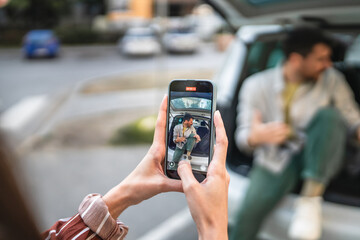 woman record a video of man tourist blogger while sit on the car trunk