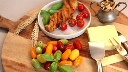 Healthy breakfast Mixed colorful tomatoes, cherry tomatoes, cheese slice, breadstick, basil leaves on wooden board arranged for simple, healthy, rustic eco-friendly clean eating food concept.