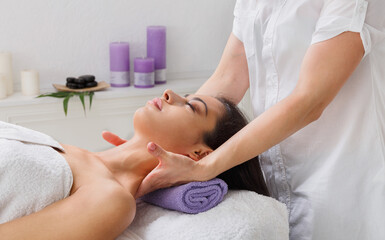 Neck massage in spa. Female beautician doctor with patient in wellness center. Professional cosmetologist make procedure to beautiful indian girl in cosmetology cabinet or beauty parlor.