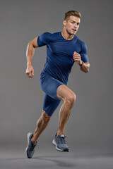 Handsome caucasian man running, wearing short sleeve shirt and shorts, sports running, fitness, gray background