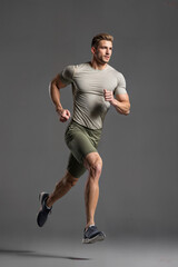 Handsome caucasian man running, wearing short sleeve shirt and shorts, sports running, fitness, gray background