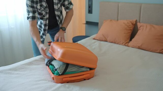 Man trying to close over packed orange suitcase before trip. Male traveler has trouble while packing a lot of clothes, preparing for travel