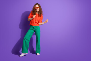 Cheerful young woman with a radiant smile posing confidently against a vibrant purple backdrop wearing trendy and stylish casual attire.