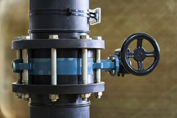 Detailed Close-up of a Black Industrial Pipe with a Blue Flanged Valve and Handwheel for Manual Flow Control