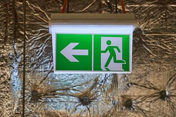 Illuminated Green and White Emergency Exit Sign with Arrow Pointing Left and Running Man Pictogram Mounted on a Wall