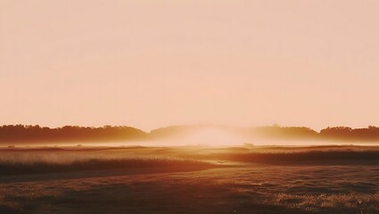 Fototapeta premium A serene landscape bathed in the soft glow of dawn, with mist gently drifting across the fields and trees silhouetted against the warm sky.