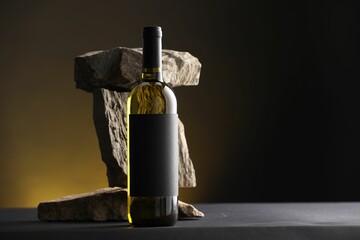 Bottle of wine and rocks on black table against dark yellow background, space for text