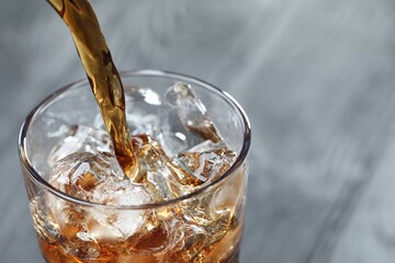 Pouring refreshing cola into glass on blurred grey background, closeup. Space for text