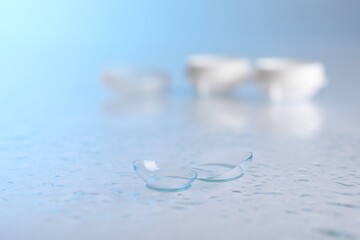 Pair of contact lenses, container and water drops on light mirror surface, selective focus