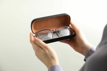 Woman holding case with stylish glasses and cleaning cloth on light background, closeup
