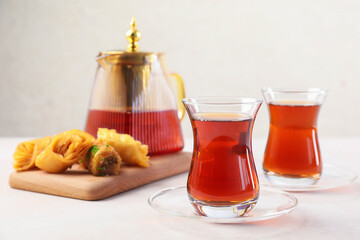 Traditional Turkish tea in glass cups, teapot and fresh baklava on white table, closeup