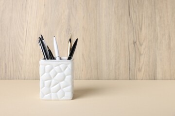Ballpoint pens in holder on beige table against wooden background. Space for text