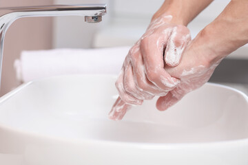 Woman washing her hands with foaming soap above sink in bathroom, closeup