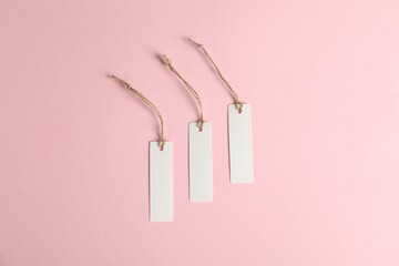 Blank tags with strings on pink background, flat lay