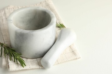 Marble mortar with rosemary, pestle and cloth on white table, closeup. Space for text