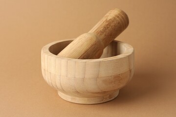 Wooden mortar and pestle on light brown background, closeup