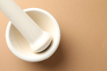 Ceramic mortar and pestle on light brown background, top view. Space for text