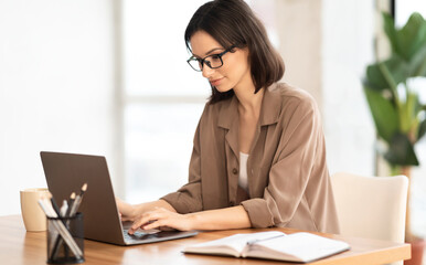 Pensive Worker. Portrait of smiling girl in eyeglasses using laptop, sitting at office and doing research, copyspace